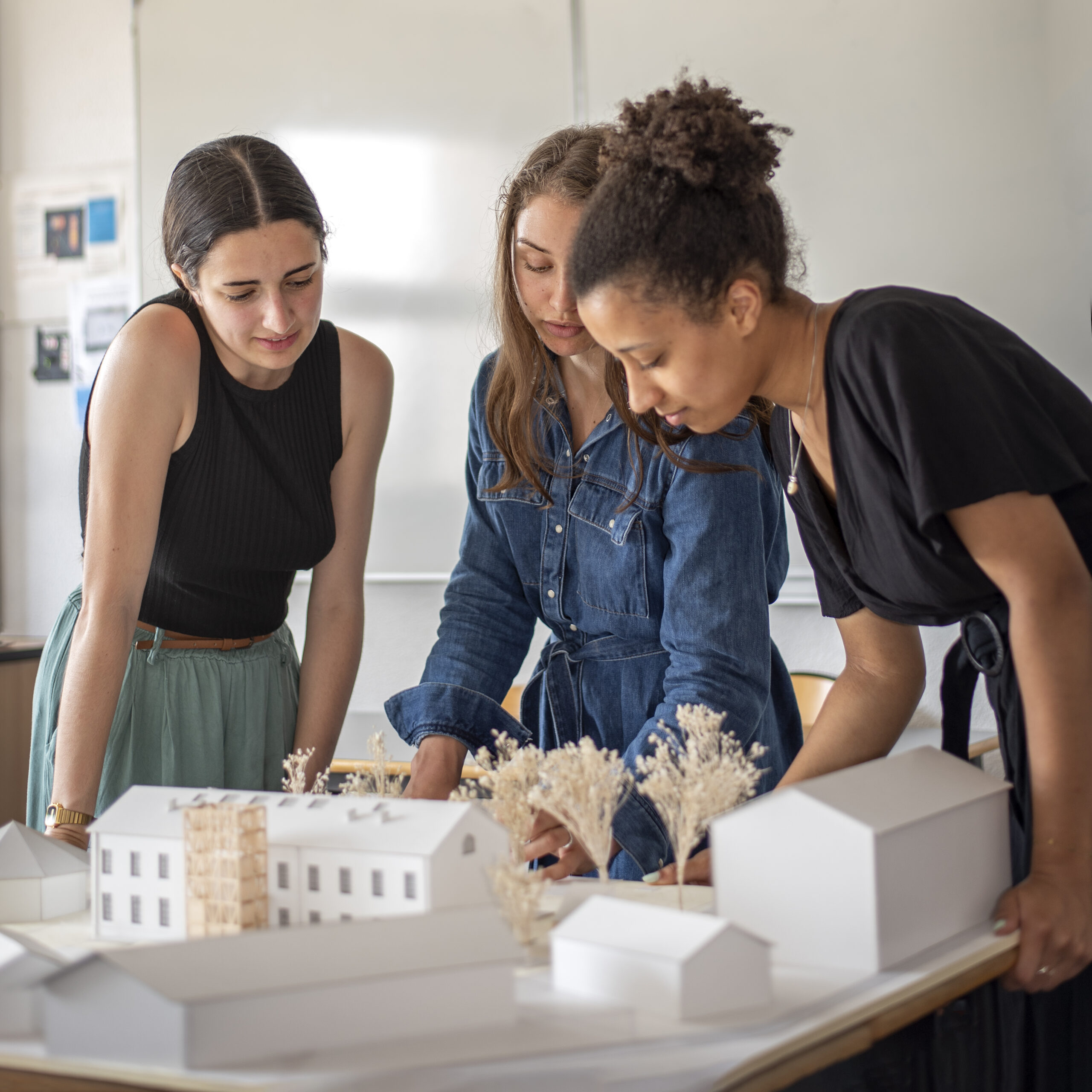 3 femmes qui regarde une maquette de batiment sur une table