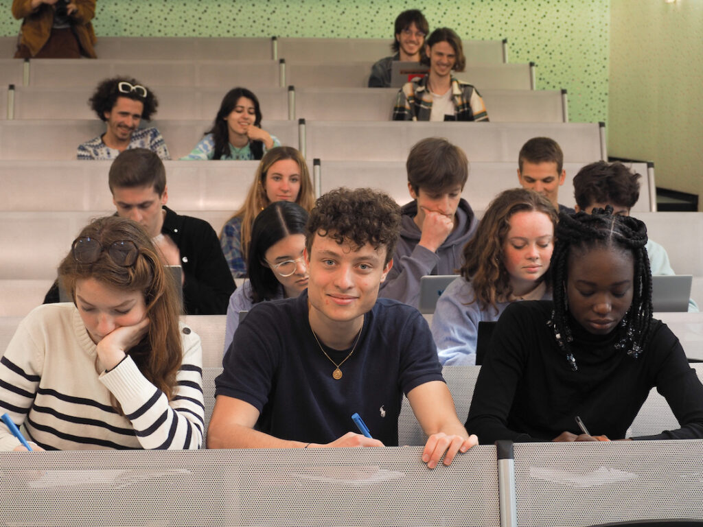 Des élèves assis dans un amphithéatre, qui sourient ou travaillent