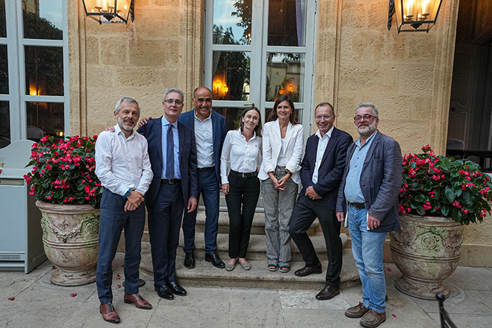 7 personnes, dont 2 femmes, tous en chemise devant la porte d'un bâtiment