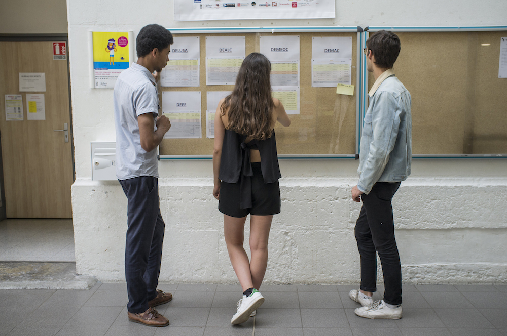3 élèves de dos qui regardent des affiches avec des noms sur le mur