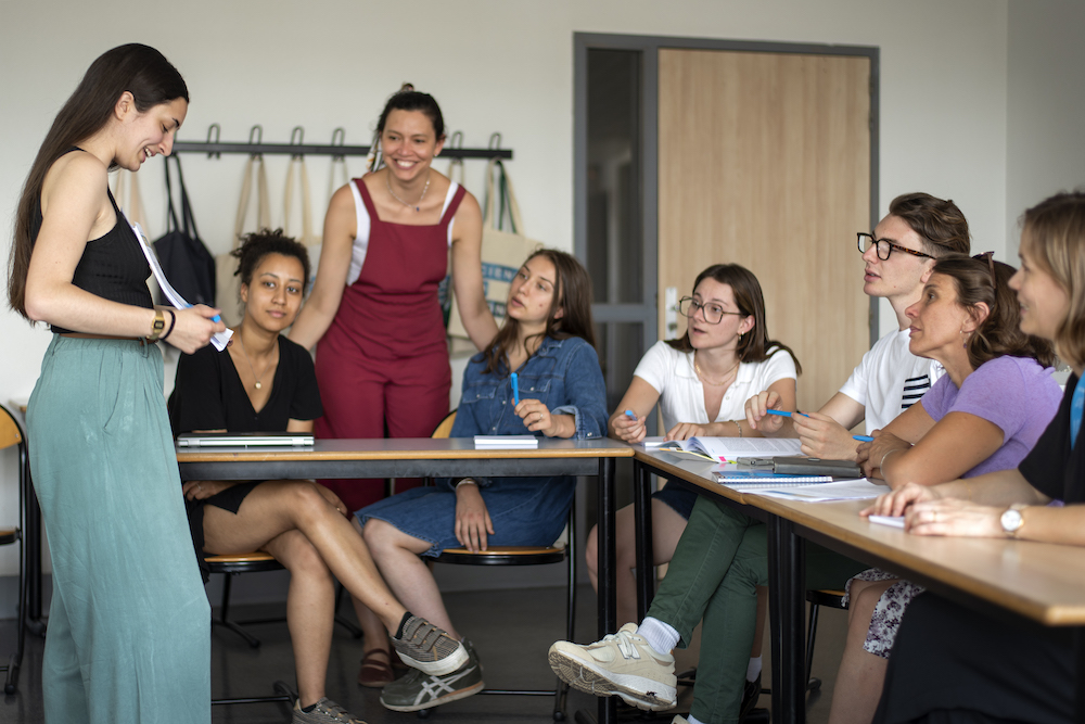 Une élève qui parle devant des élèves sur une table en forme de U