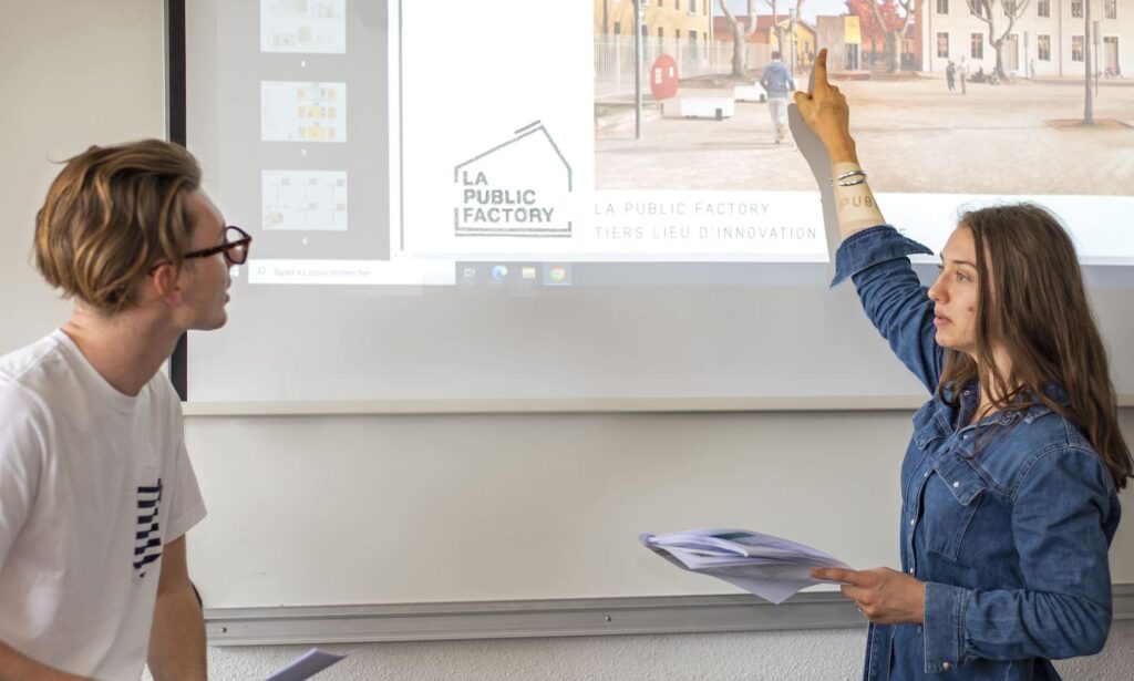 Deux élèves qui devant une présentation sur vidéo projecteur. La fille montre du doigt quelque chose sur l'image projetée au tableau
