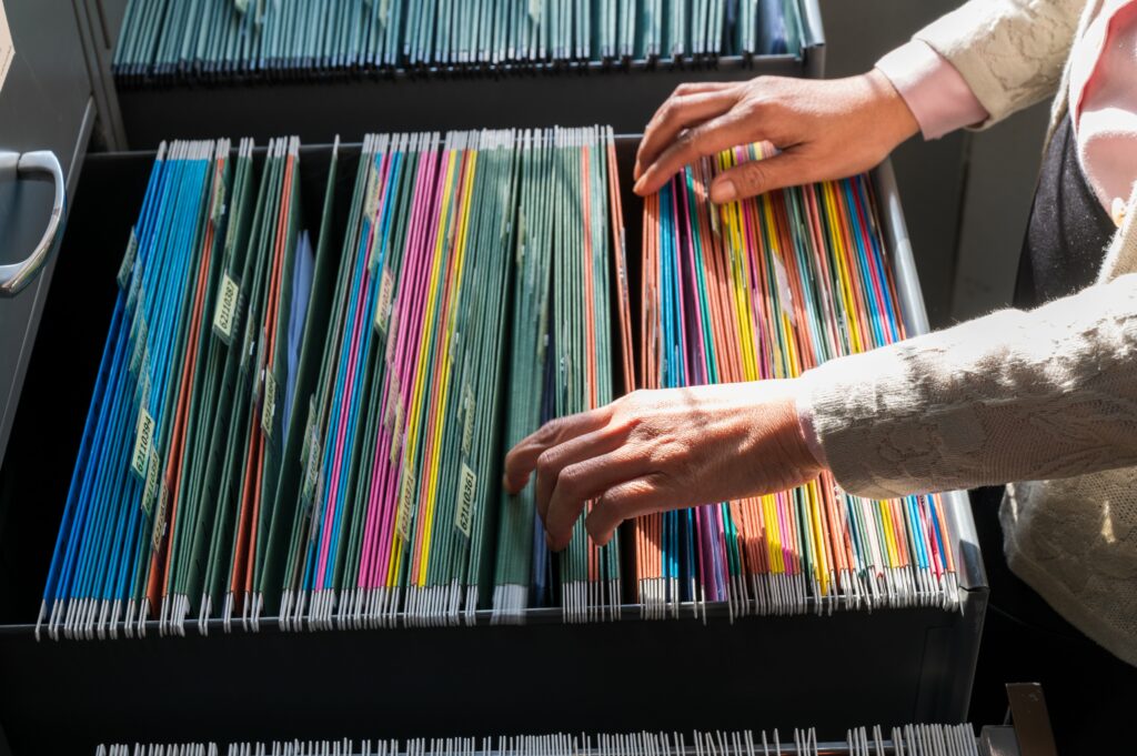 Plan sur des dossiers de couleurs dans un tiroir, avec un gros plan sur deux mains qui sont en train les toucher