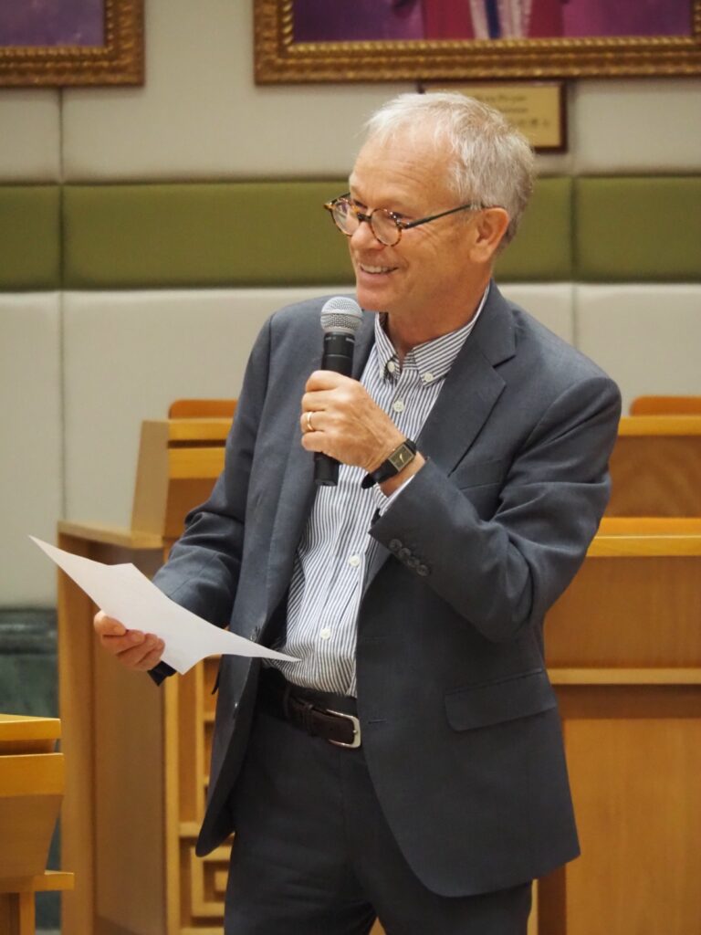 Professeur qui parle avec un micro dans la main, et une feuille dans l'autre