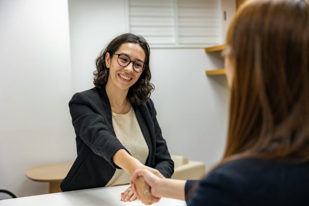 Une femme qui sers la main à une autre femme, de dos.
